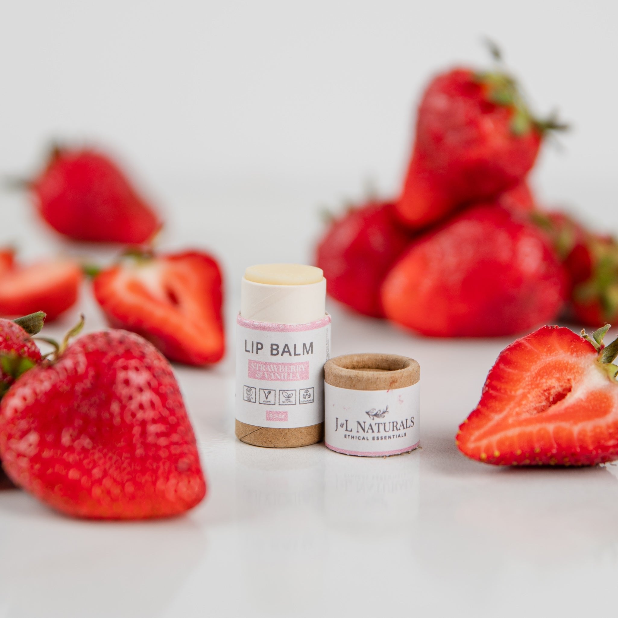 Two lip balm sticks paired with fresh strawberries and a bright, clean background.