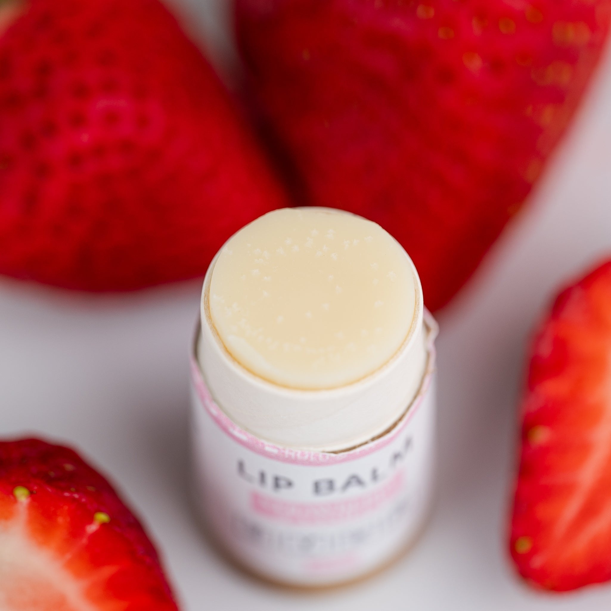 A close-up of lip balm sticks displayed with strawberries for a natural, sweet aesthetic.