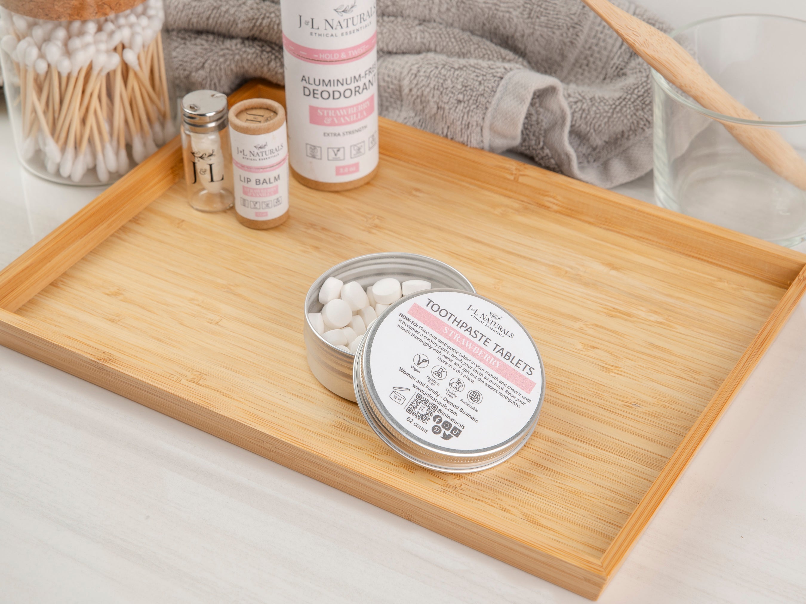 A bamboo tray holding a tin of toothpaste tablets with eco-friendly dental care items, including a toothbrush, floss, and cotton buds in a minimalist setting