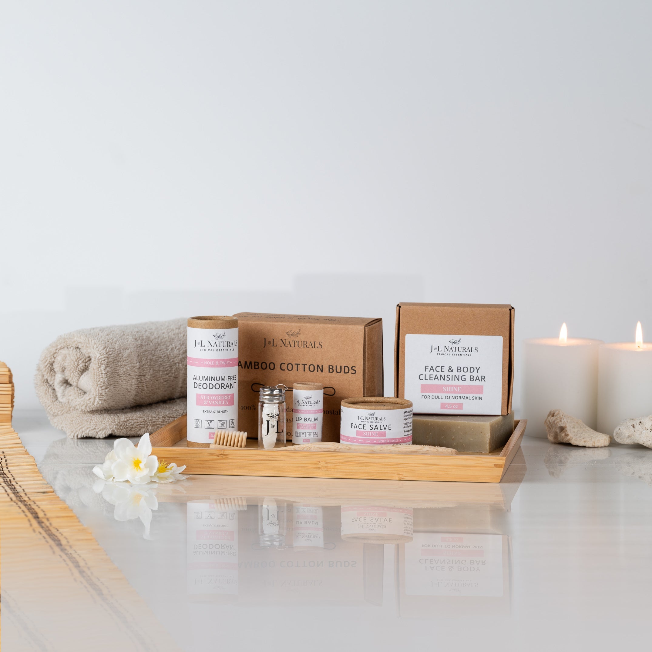 products displayed on table, candles and rolled towel on sides with flowers, white background