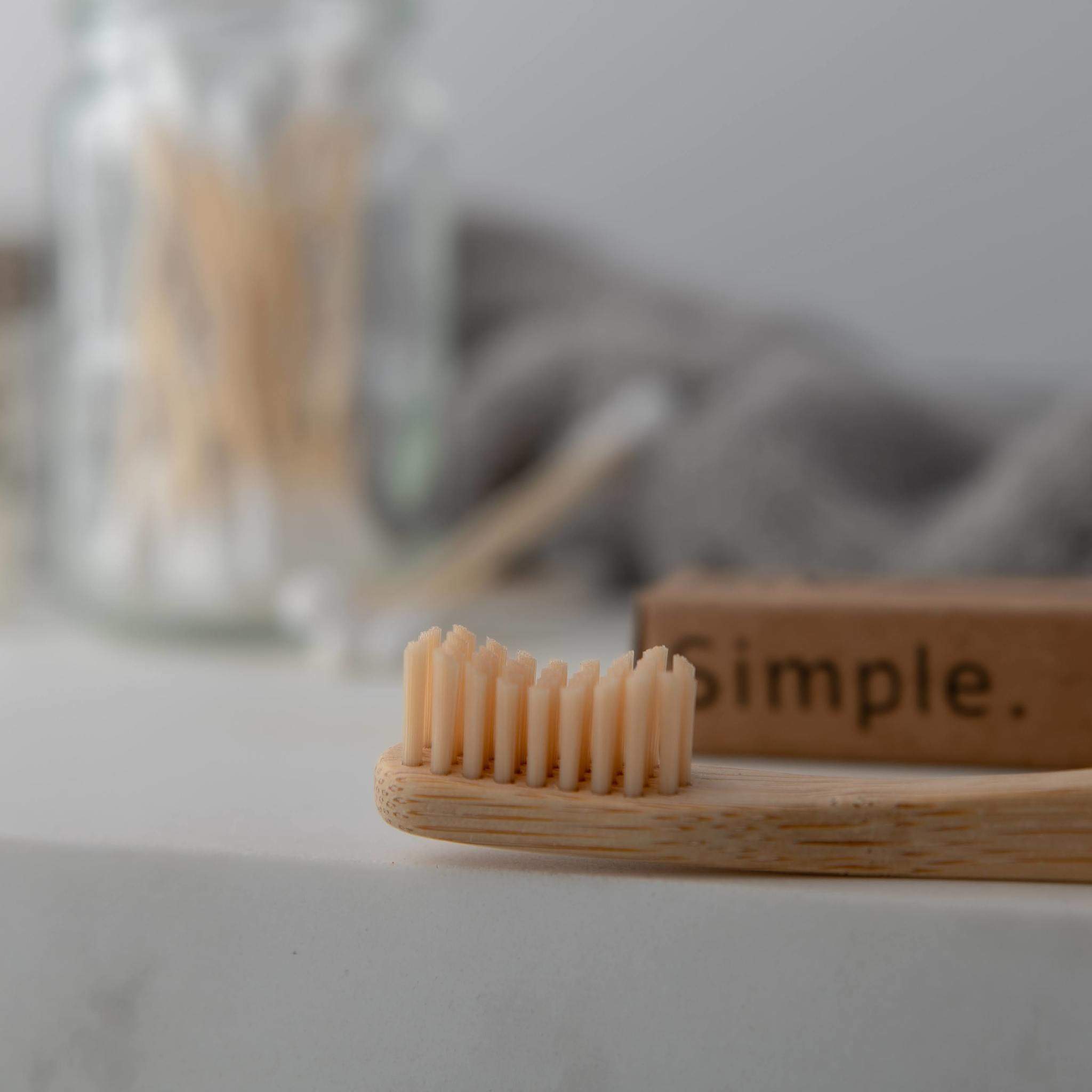 A bamboo toothbrush resting on a wooden holder, with a jar of swabs blurred in the background.