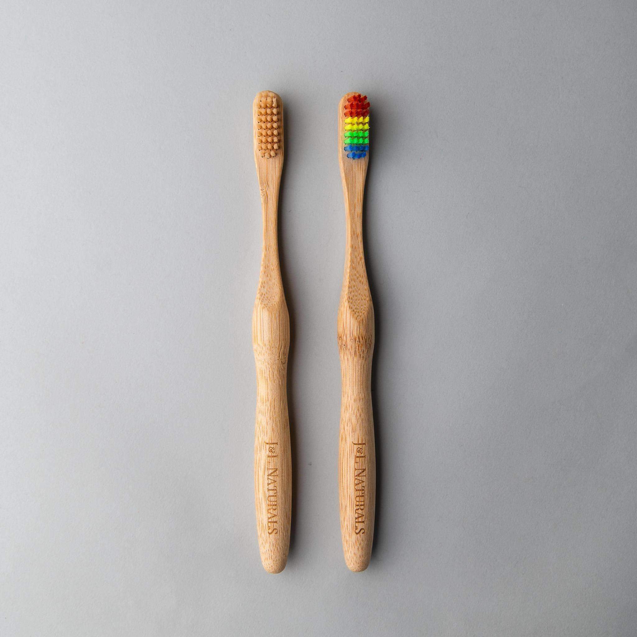 A pair of bamboo toothbrushes with natural and rainbow bristles, displayed on a smooth gray background.