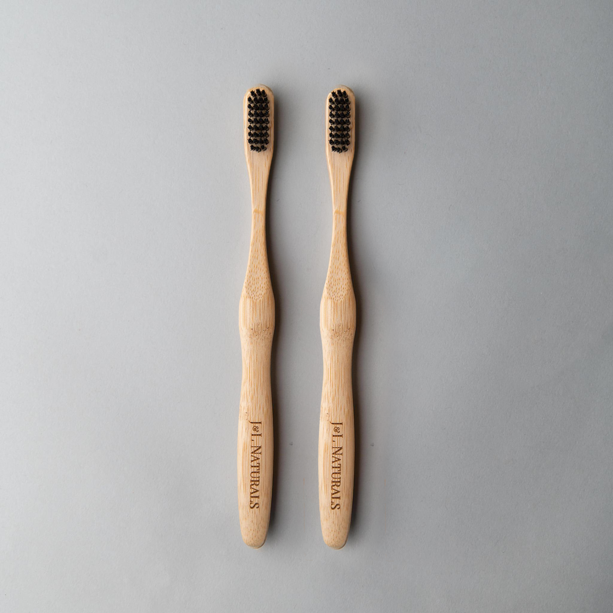 Two bamboo toothbrushes with black bristles, arranged side by side on a gray background.