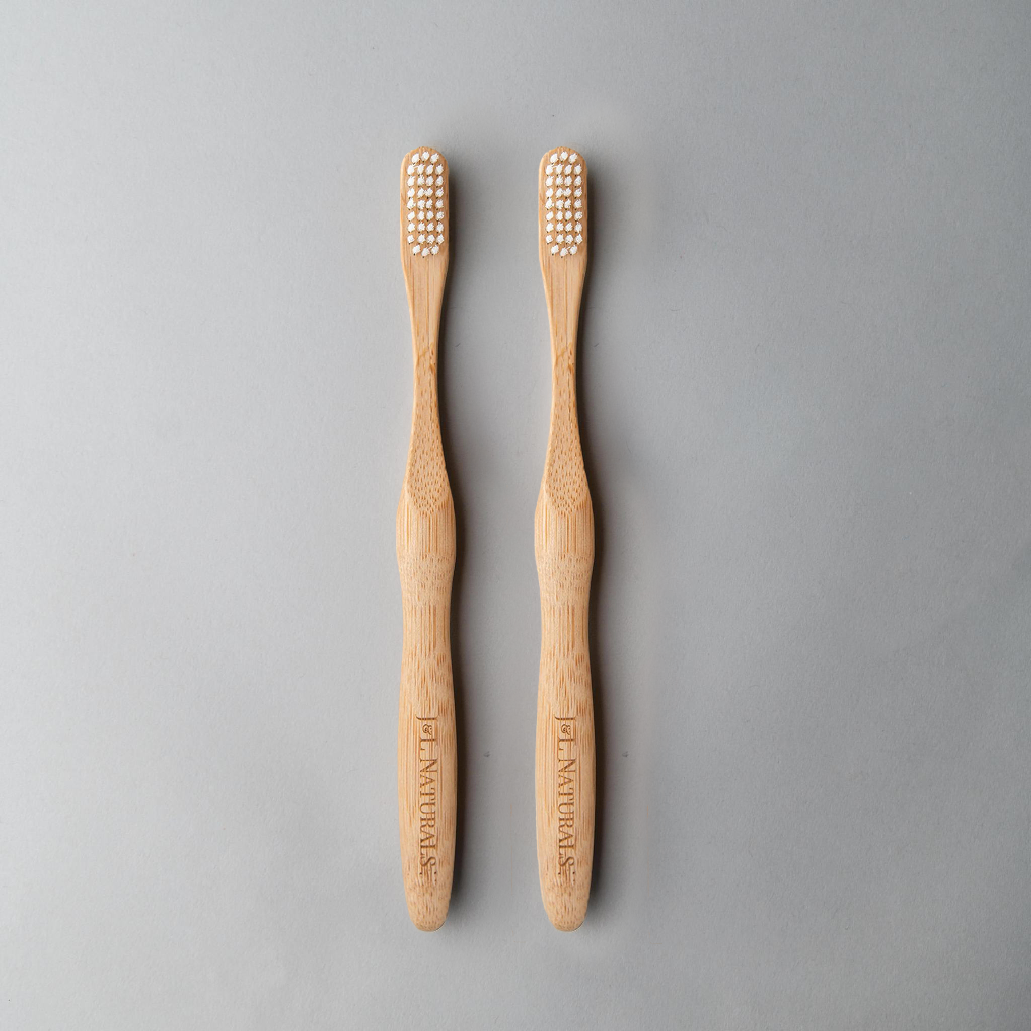 Two bamboo toothbrushes with white bristles, arranged side by side on a gray background.