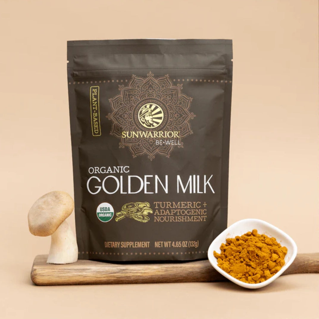 golden milk package on wooden board with mushroom on left and small dish of orange powder on the right. plane tan background