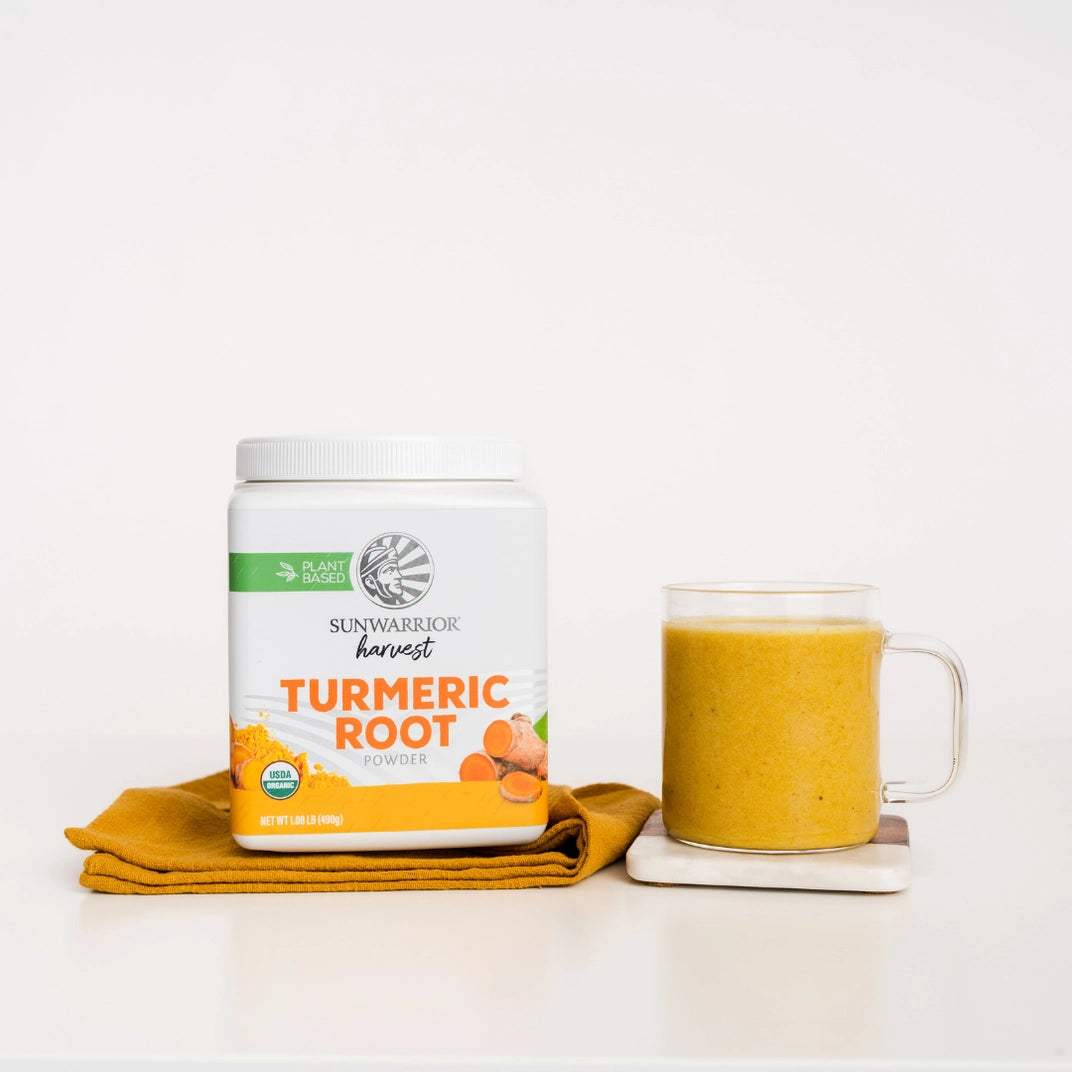 turmeric root container on an orange towel, next to  glass of orange liquid on a saucer, white background