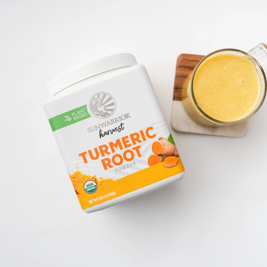 looking down on turmeric container front next to glass of orange liquid on a saucer with white background