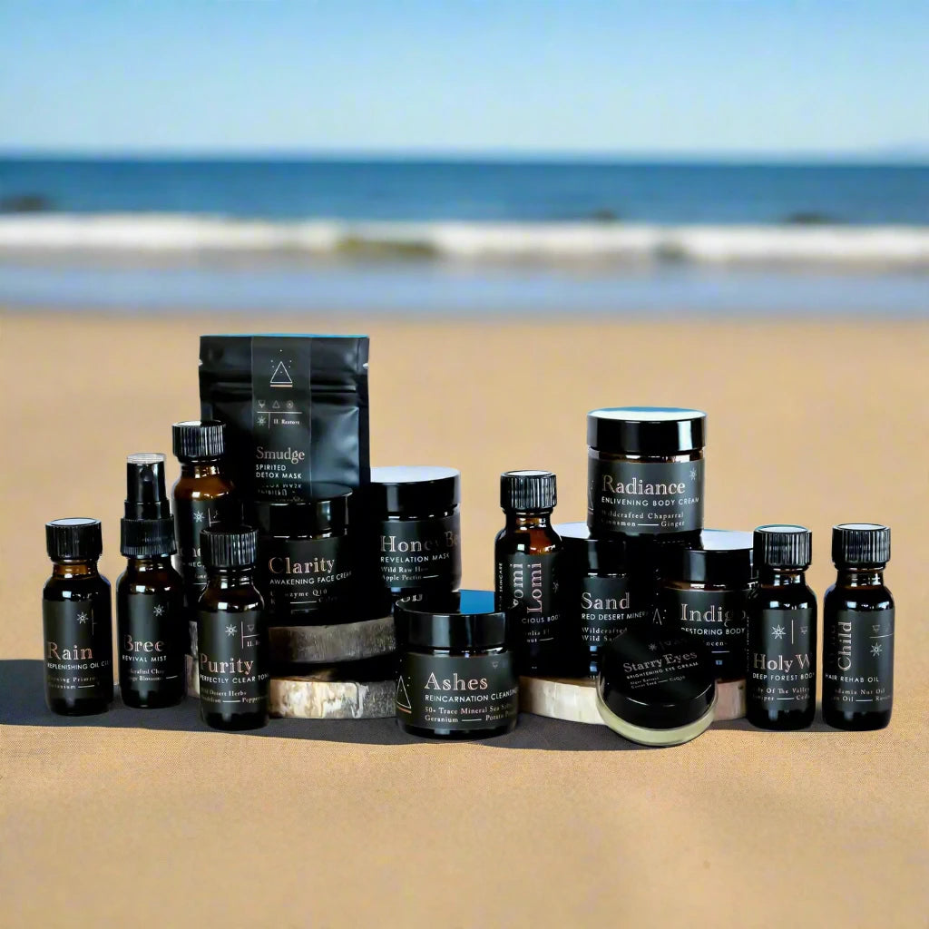 all product bottles displayed on a table with 2 discs raising some products on beach sand, bright warm sun, oregon coast, blue sky, ocean waves