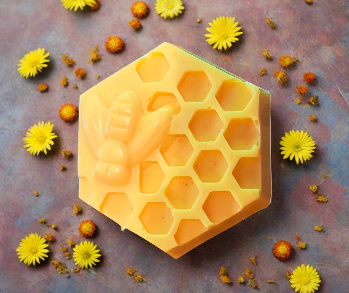 hexagon shaped bar soap with honeycomb cut out and raised honey bee on stone with yellow and orange flowers scattered around it.