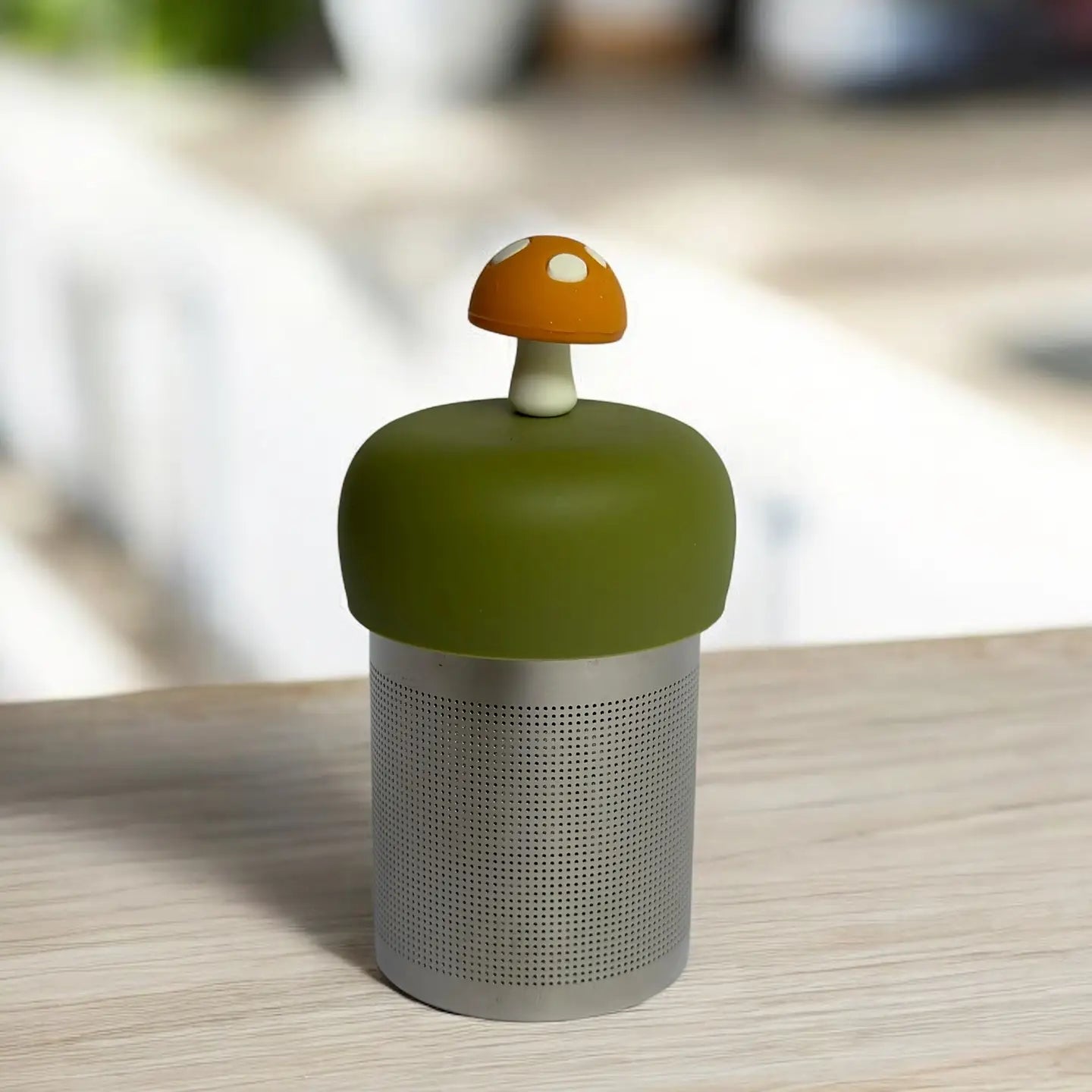 steel mesh tea strainer with green mound top and mushroom top on a table