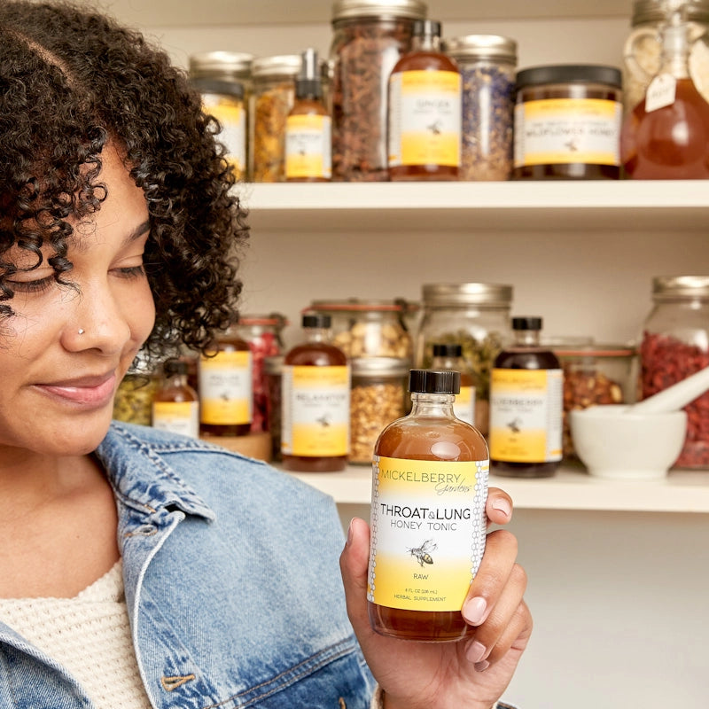 woman holding bottle of tonic and shelves with jars behind