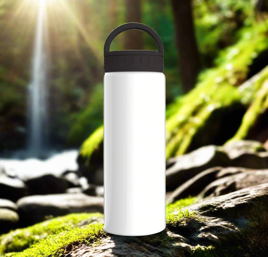 A crisp white water bottle on rocks by a stream, with a cascading waterfall and sunlight filtering through the trees in the background.