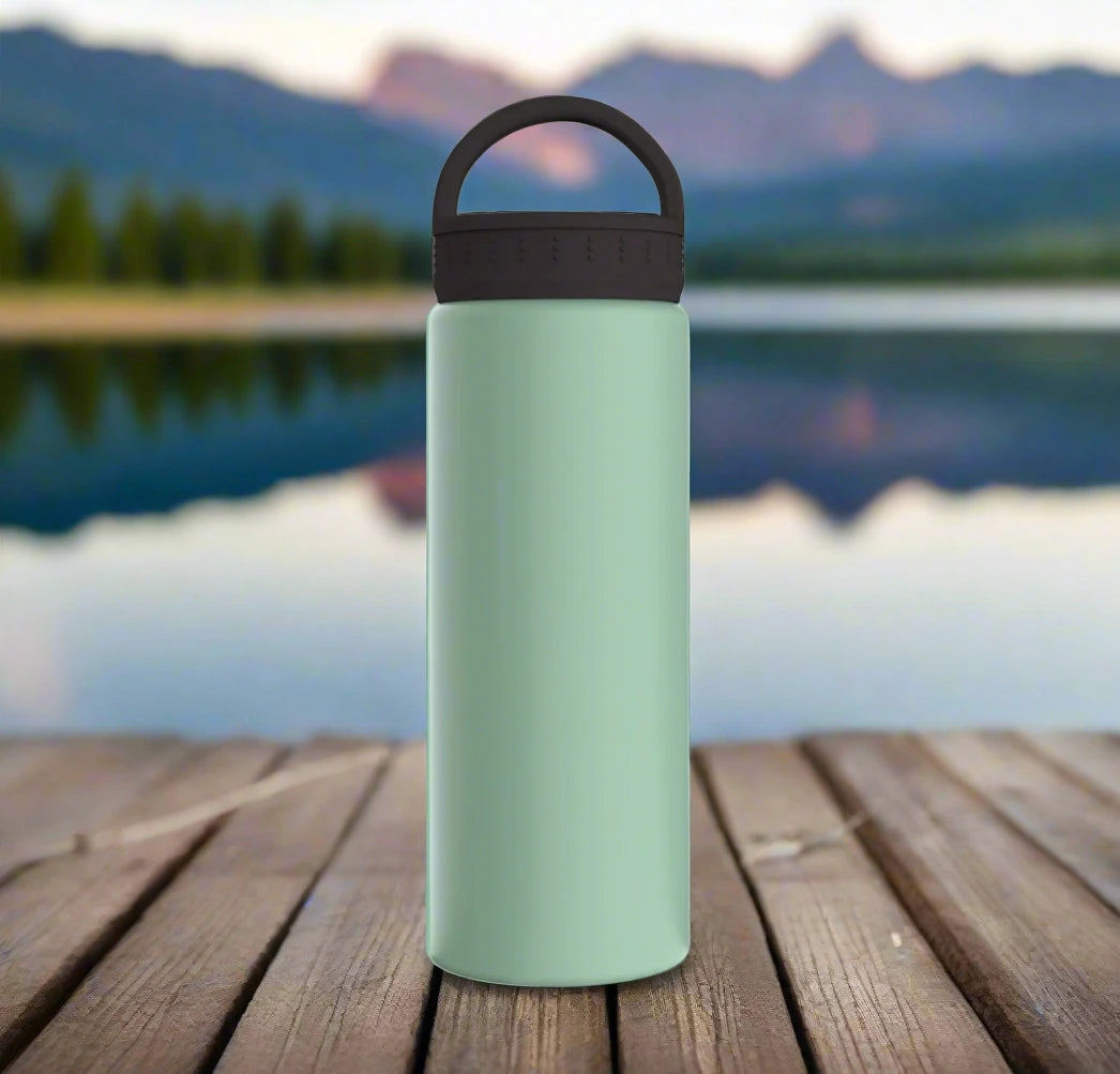 A light green water bottle resting on a dock, overlooking a serene lake with majestic mountains in the distance.